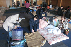 女性警察官が避難所で避難住民の寝具を片付けている様子